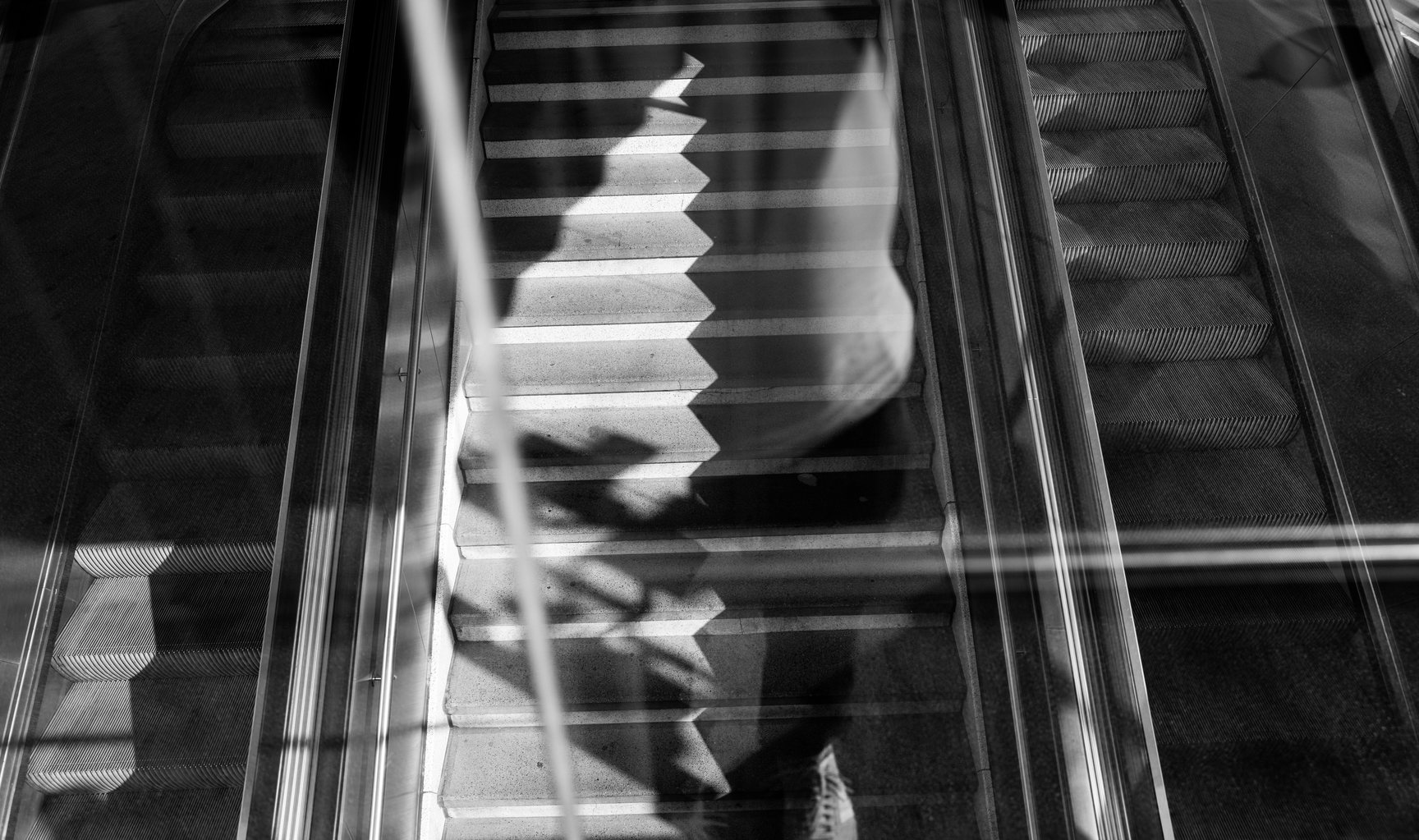 Spiegelung einer Person auf einer Rolltreppe, Schwarzweißfotografie.